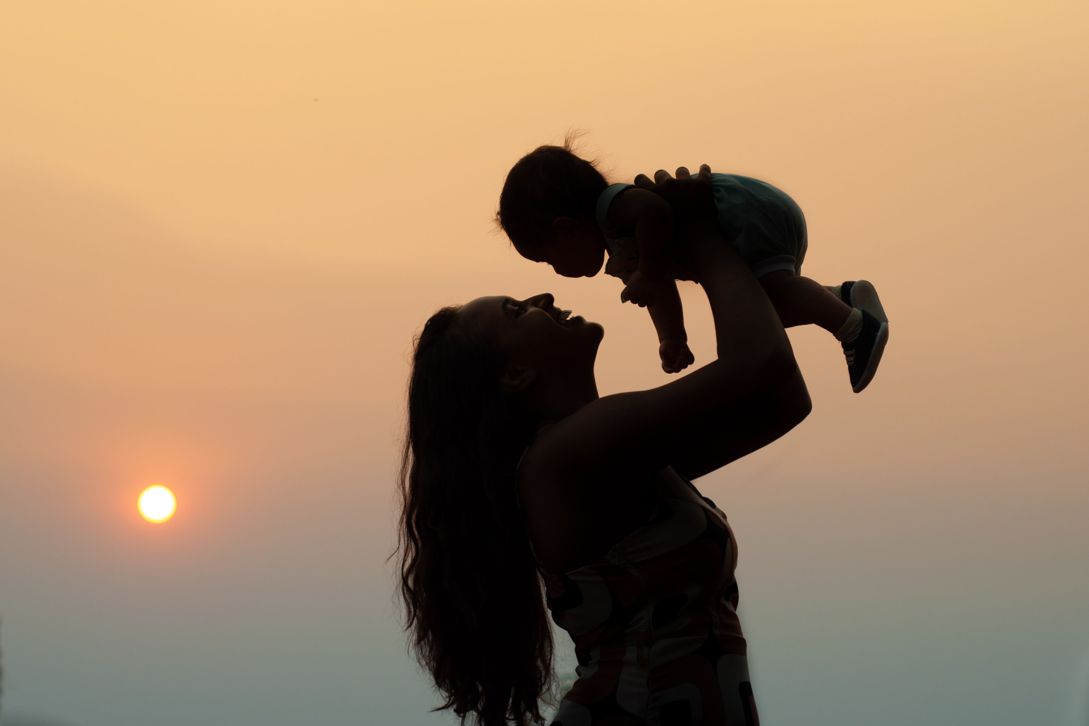 Silhouette of a mother lifting her child against a warm sunset sky